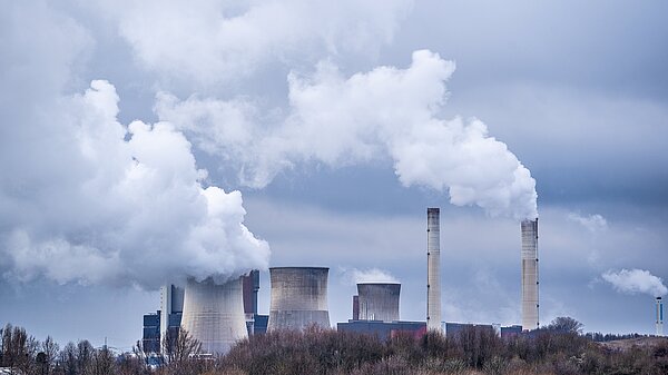 A power station with smoke blowing out of the chimneys.